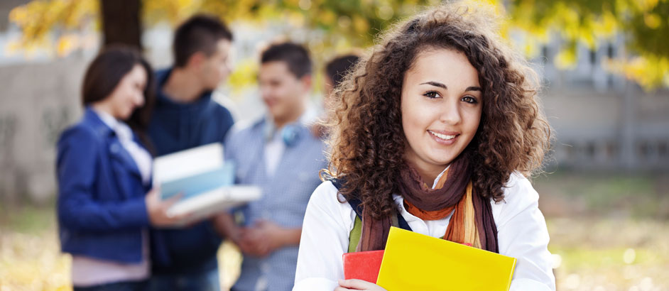 Eine Studentin blickt in die Kamera, im Hintergrund ist eine Gruppe von Studierenden