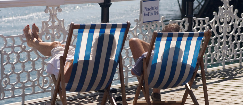 Zwei Personen sitzen in Sonnenstühlen auf einer Strandpromenade