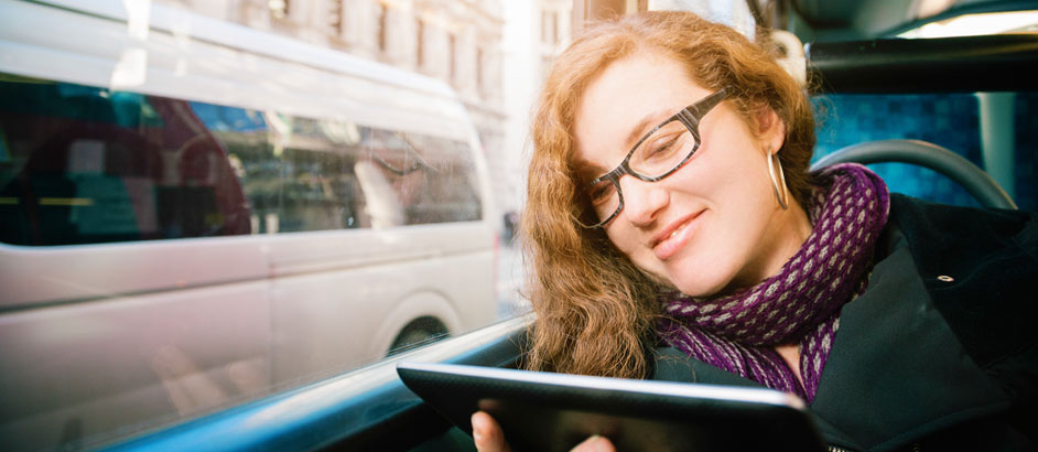 Junge Frau sitzt in einem Bus am Fenster und schaut auf ein Tablet.