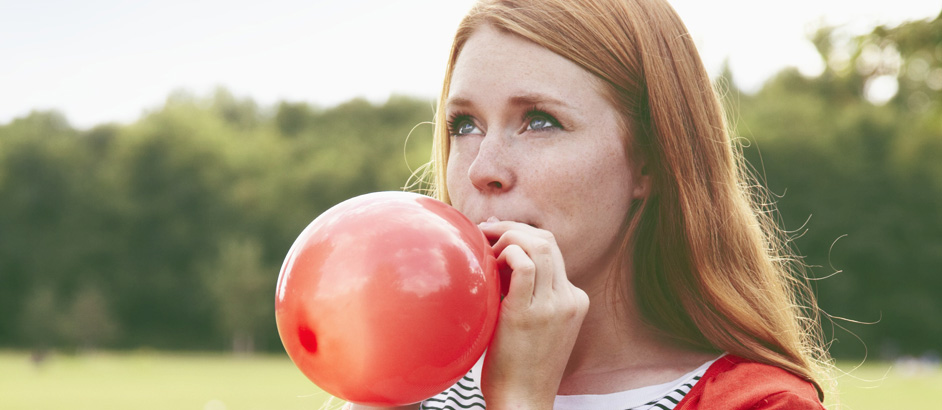 Rothaarige junge Frau bläst einen roten Luftballon auf.