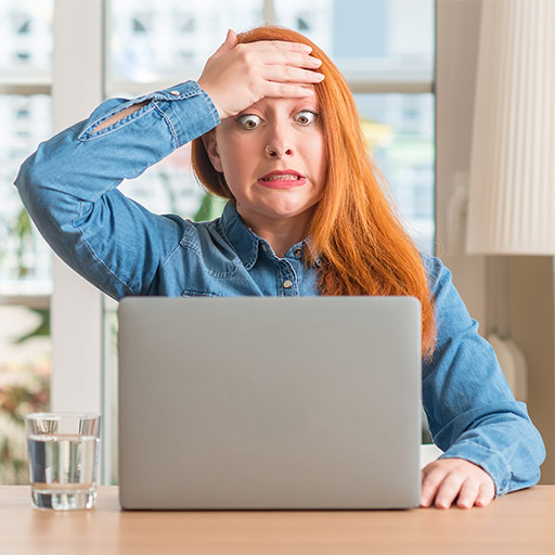 Eine junge Frau blickt entsetzt auf ihren Laptop und schlägt sich mit der Hand auf die Stirn.