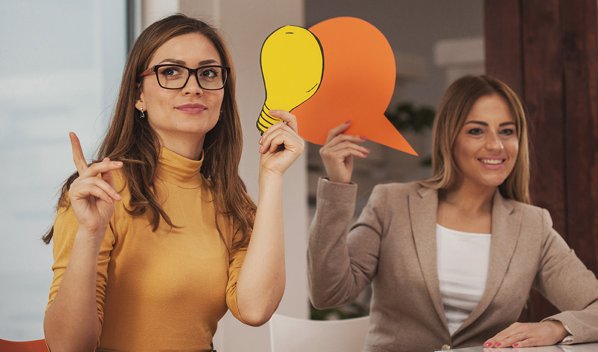 Zewei junge Frauen agieren mit großenSprechblasen aus Pappe.