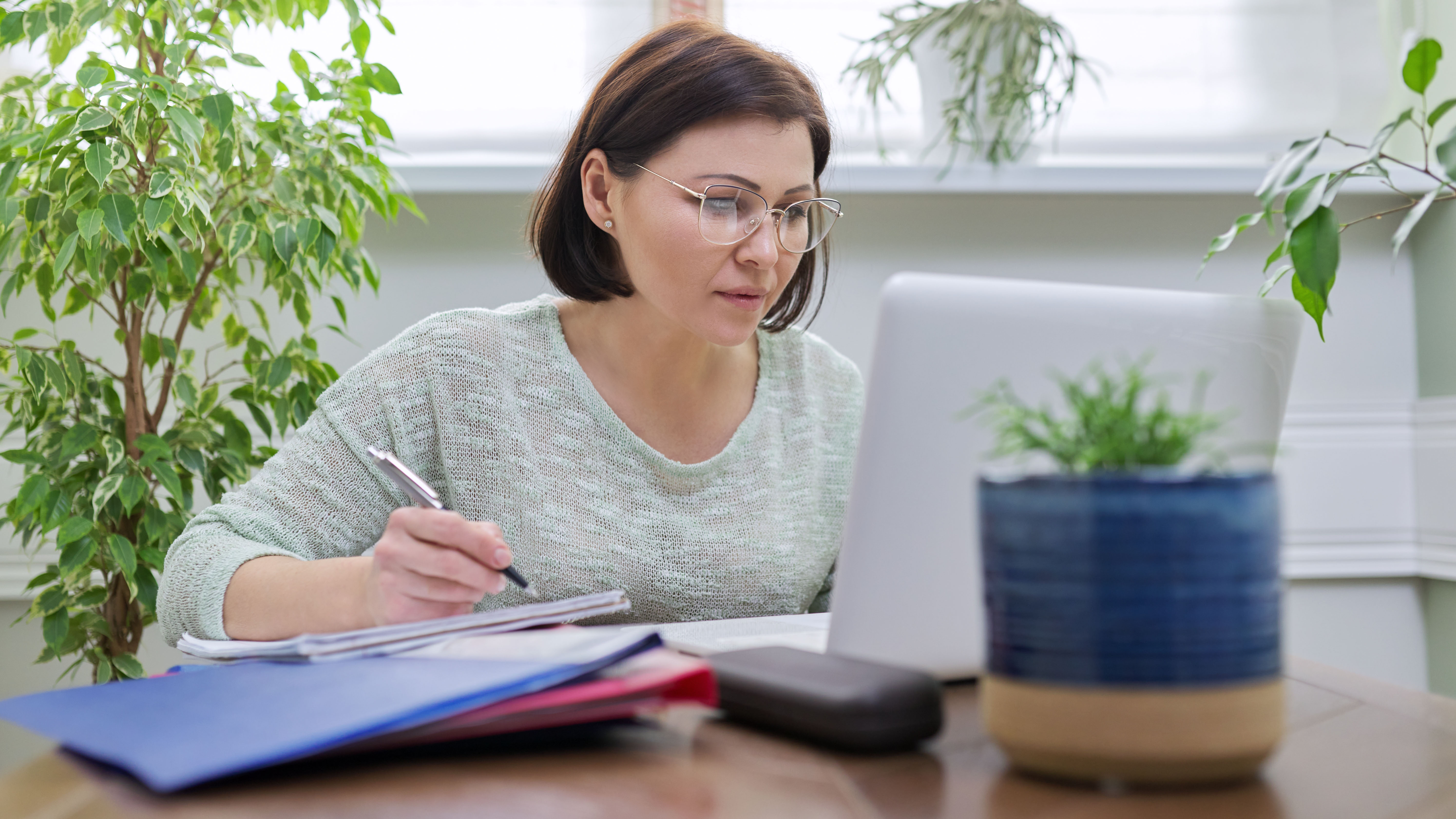 Eine Frau sitzt vor einem Laptop am Tisch und arbeitet.