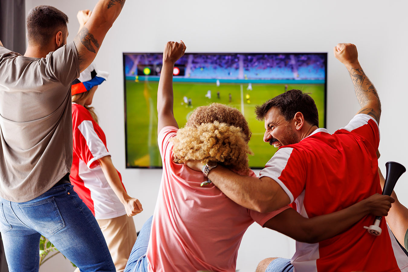 Eine Gruppe Menschen schaut im Fernsehen ein Fußballspiel und feiert ein Tor.