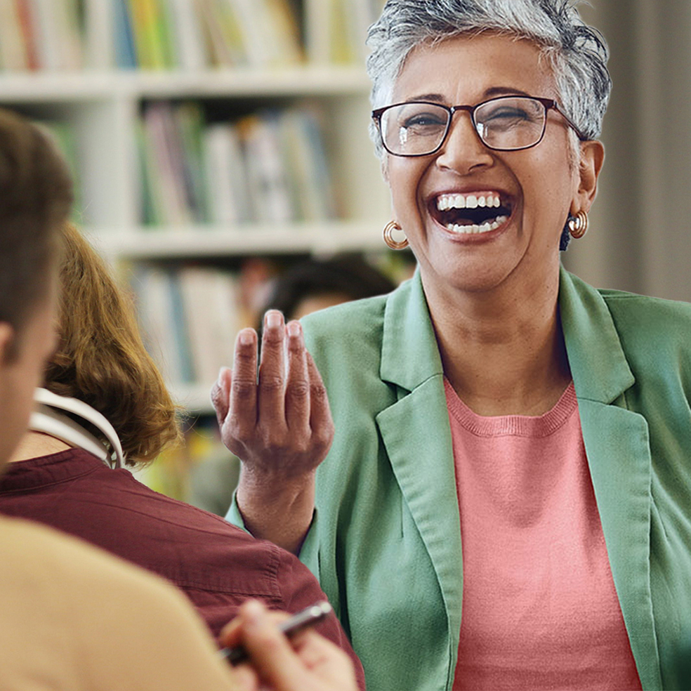Eine ältere Lehrerin steht vor einer Klasse und lacht