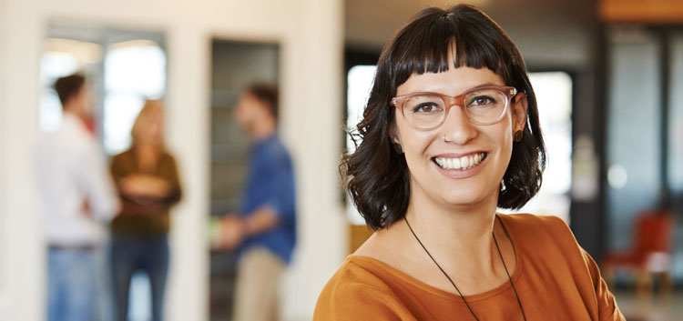 Brünette Frau mit Brille lächelt in die Kamera.