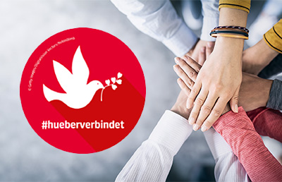 Hände eines Teams liegen aufeinander, daneben ist das Logo von #hueberverbindet mit einer weißen Friedenstaube