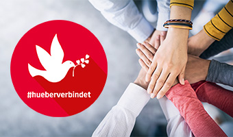 Ein Team legt die Hände aufeinander. Daneben ist ein roter Button mit einer Friedenstaube und dem Hashtag #hueberverbindet