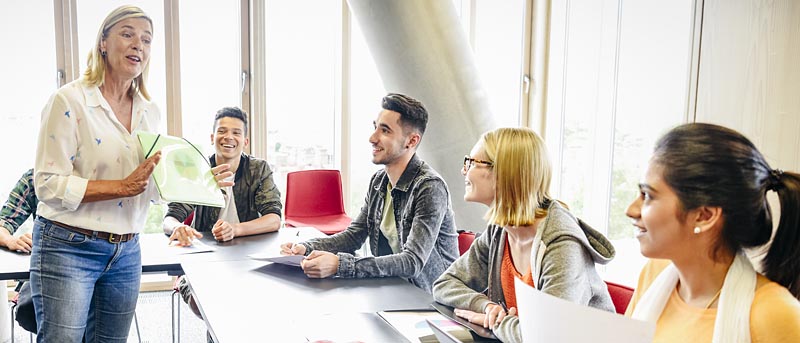 Lehrerin hält in der Hand eine Blatt, das sie Studenten erklärt.