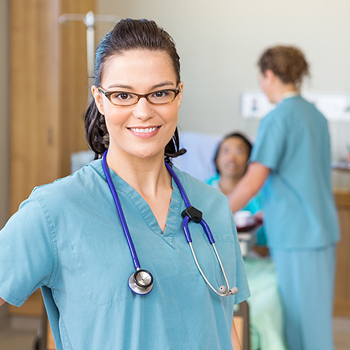 Eine Krankenschwester steht vor einem Patientenbett und lächelt in die Kamera.