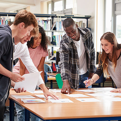 Schüler:innen stehen um einen Tisch und bereiten im Unterricht ein Projekt vor.