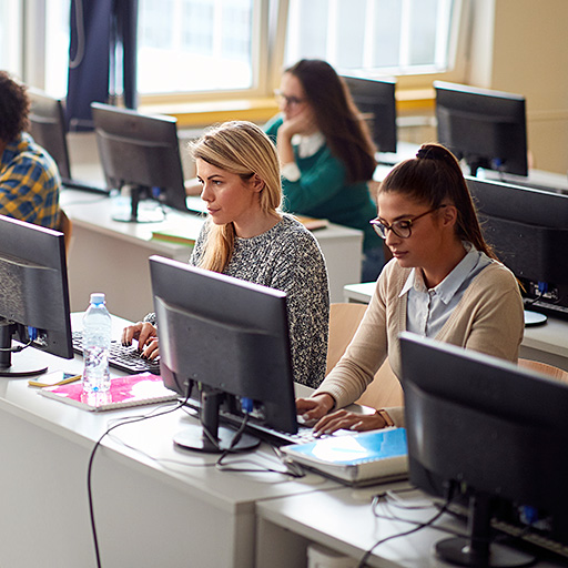 drei Frauen sitzen in einem Computerraum und arbeiten