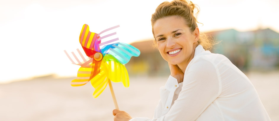 Eine Frau sitzt am Strand und hält ein Windrad in der Hand