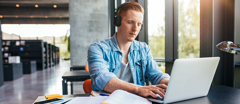 Student sitzt in der Bibliothek und tippt in seinen Laptop